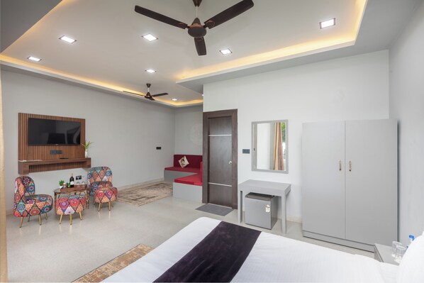 A modern hotel room with a bed, a desk, a wardrobe, a seating area with chairs, and a ceiling fan. - Amadi Beach Front Resort (Ashvem)