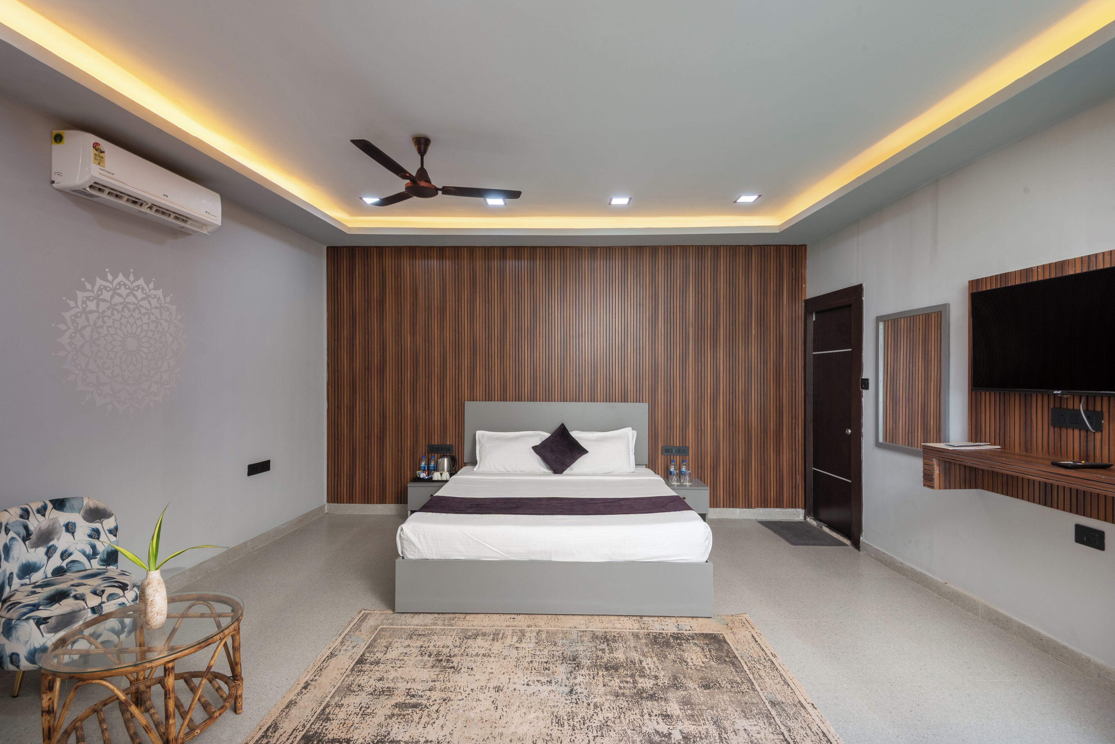 A modern bedroom with a bed, bedside tables, a ceiling fan, an air conditioner, a TV, and a decorative wall panel.