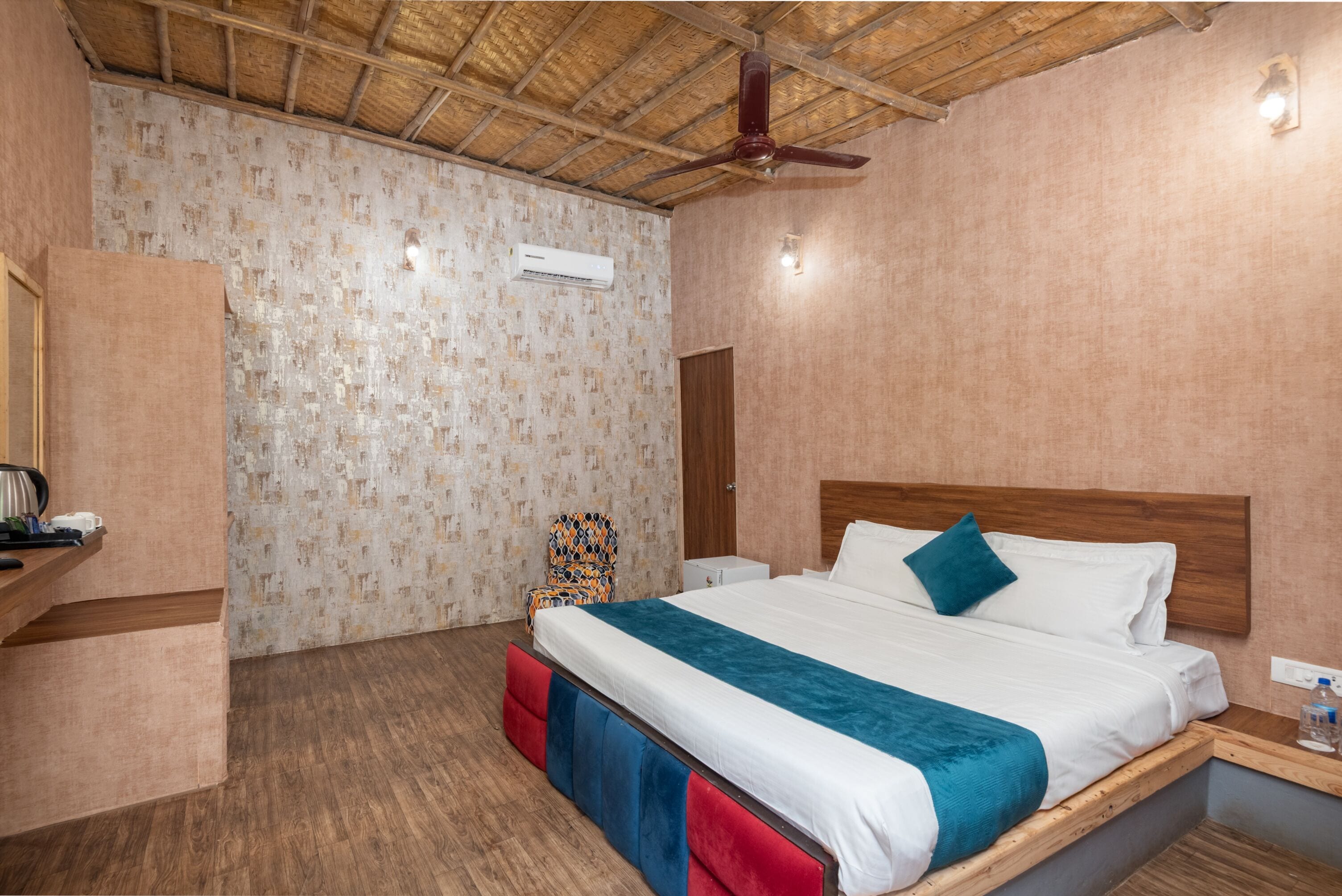 A bedroom with a wooden ceiling, a bed with a teal blanket, a wooden nightstand, a chair, and a wardrobe.