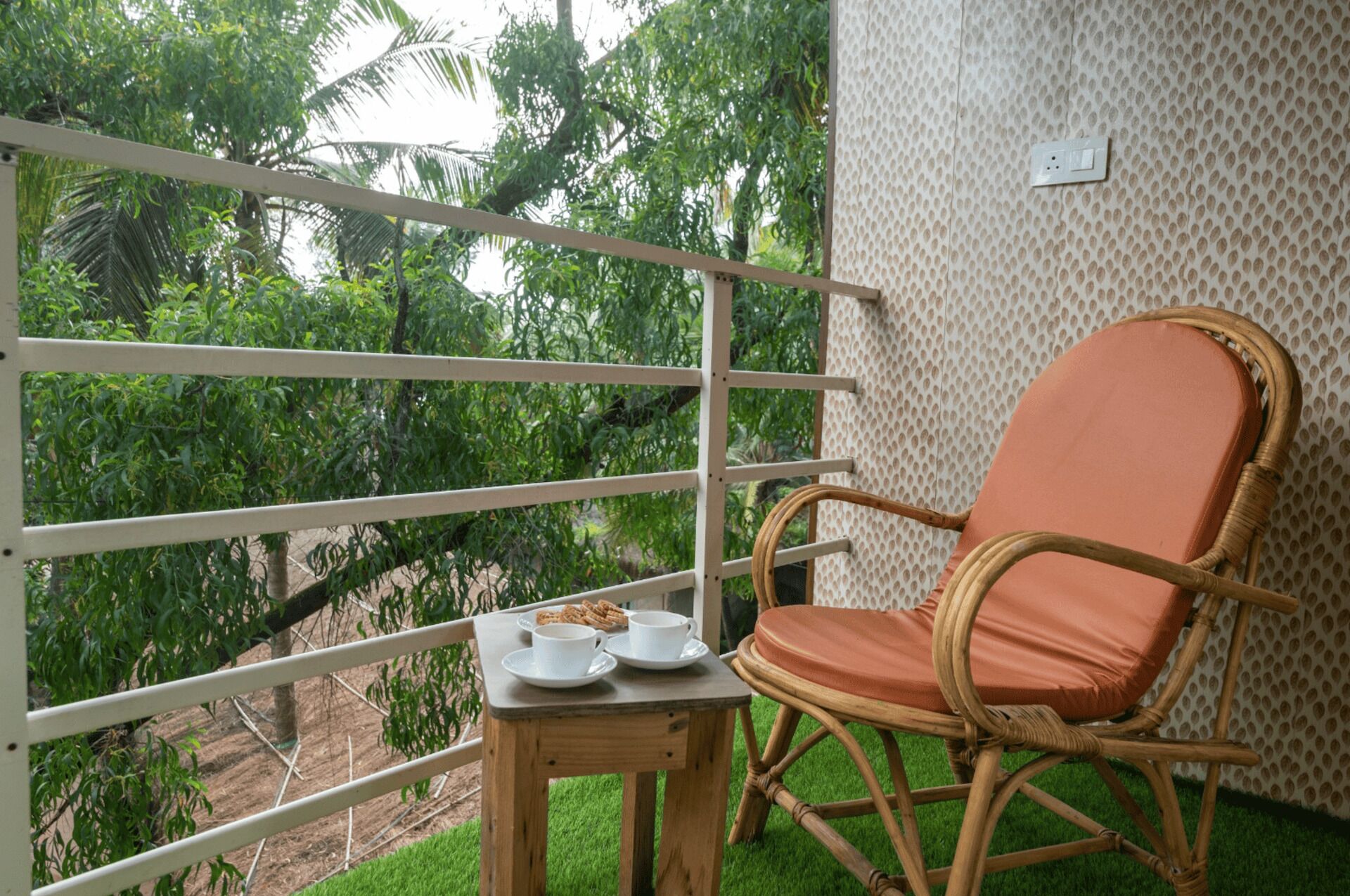 Une chaise en osier avec un coussin, une petite table avec une tasse et une assiette, et une balustrade de balcon.