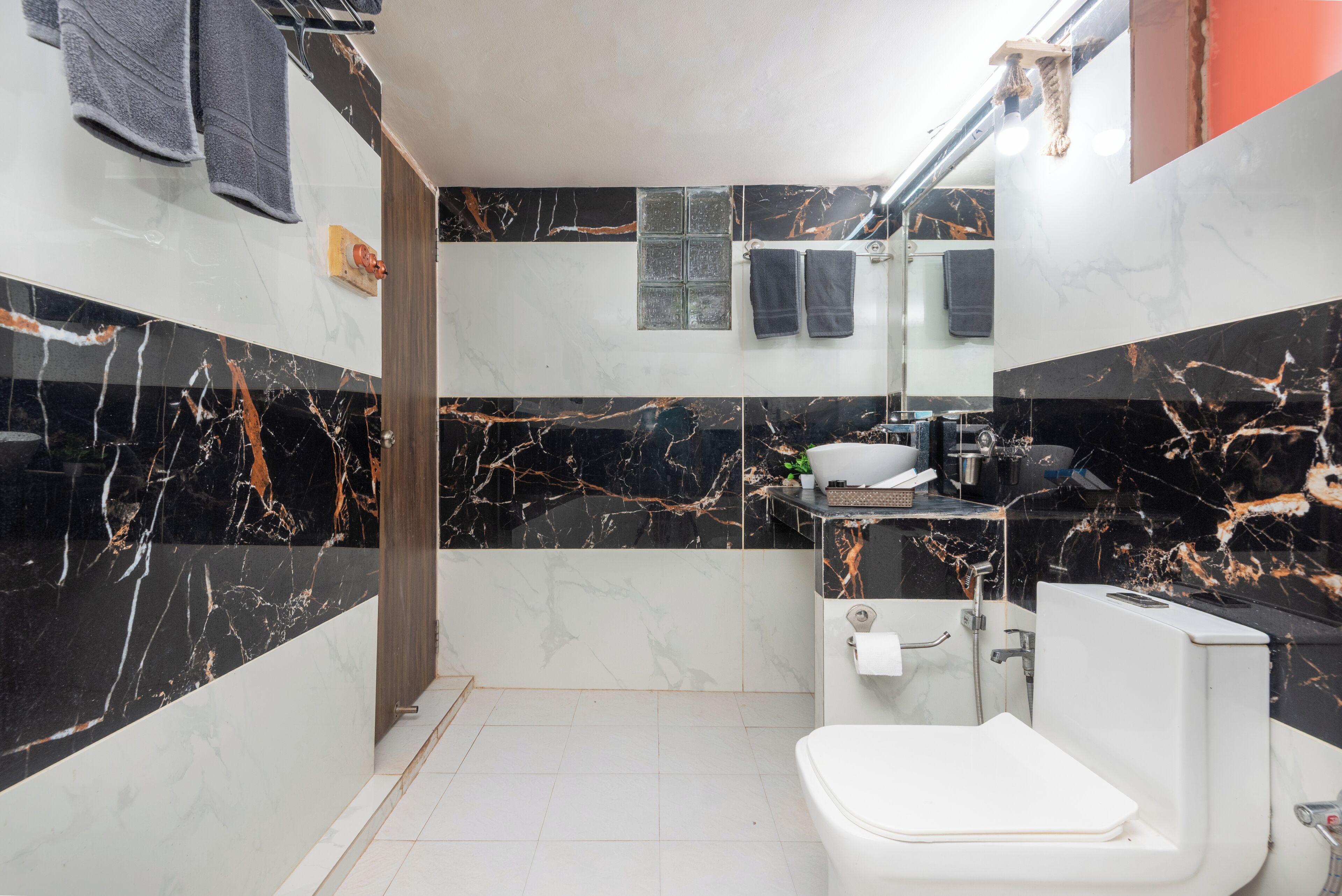 Ein modernes Badezimmer mit Toilette, schwarzen und weißen Marmorfliesen, Waschbecken mit Spiegel und Duschbereich.
