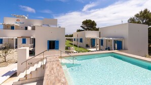 Un resort moderno con piscina, asientos al aire libre y un cielo azul despejado.