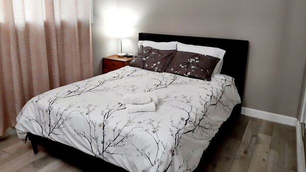 A neatly made bed with a floral bedspread, a bedside table with a lamp, and a wall with a 'love you more' sign. - Modern 4-beds House Near Disneyland & Knott's Berry Farm (Anaheim)