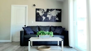 Un salon avec un canapé en cuir noir, une table basse blanche et une œuvre d’art représentant une carte du monde accrochée au mur.