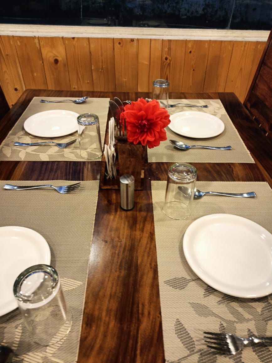 Een eettafel gedekt met borden, bestek, glazen en een rode bloemen decoratie.