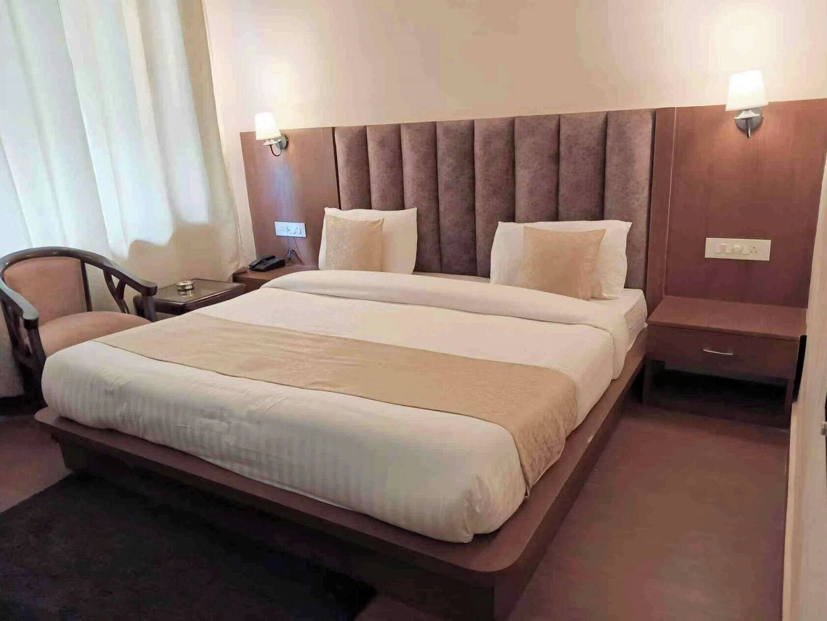 A hotel room with a large bed, bedside tables, a chair, and a nightstand.