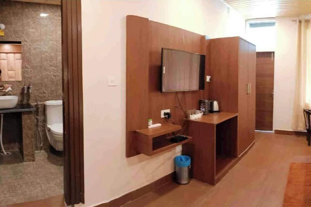 A hotel room with a bed, a TV mounted on the wall, a desk with a chair, a small table, and a window with curtains.