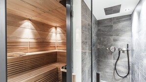 Een moderne badkamer met een houten sauna bank en een apart douchegedeelte met grijze tegels.