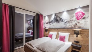 Een moderne hotelkamer met een groot bed, een houten hoofdeinde en een muurschildering van bergen en een reuzenrad.