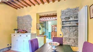 Un comedor con una mesa de madera, sillas moradas, un armario blanco y una pared de piedra.
