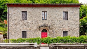 Un edificio de piedra con puerta roja, dos ventanas y un balcón pequeño.
