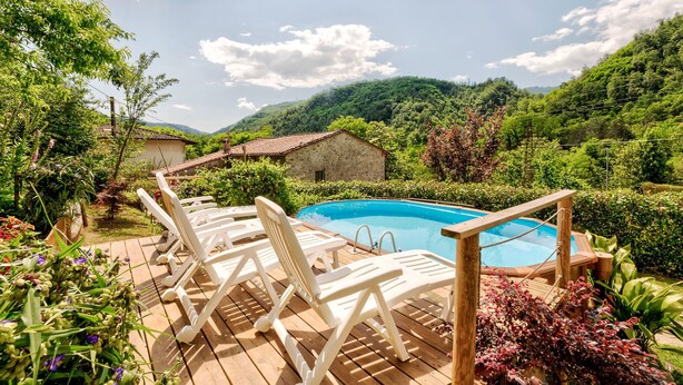 Terraza de madera con sillones de descanso y piscina rodeada de exuberante vegetación y colinas.