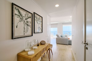 Un salón moderno con una mesa de comedor de madera, dos láminas enmarcadas con motivos botánicos y vista al océano a través de un ventanal grande.