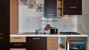Eine moderne Küche mit dunklen Holzschränken, einer weißen Arbeitsplatte, einem Edelstahl-Spülbecken, einem Gasherd und einem eingebauten Backofen.