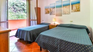 Ein Zimmer mit zwei Betten, einem kleinen Tisch und einem Fenster mit Blick auf Grün.