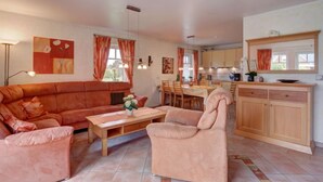 A living room with a sofa, armchair, and coffee table, a dining area with chairs and a table, and a kitchen with cabinets and a countertop. - Katamaran II by Interhome (Burhave)