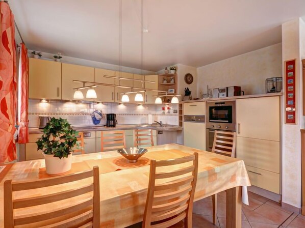 Una cocina moderna con comedor, que incluye una isla central, electrodomésticos integrados e iluminación colgante.