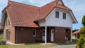 A two-story house with a red-tiled roof, a brick exterior, and a paved driveway. - Katamaran II by Interhome (Burhave)