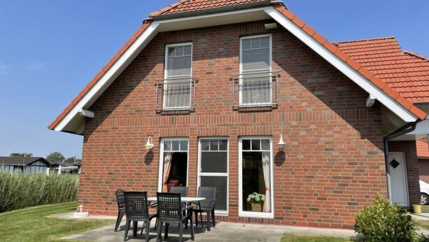 A two-story brick house with a red-tiled roof, a front porch with a table and chairs, and a small garden area. - Katamaran II by Interhome (Burhave)
