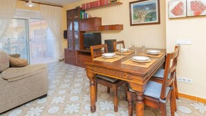 Un comedor con una mesa de madera dispuesta para cuatro personas, un sofá, un televisor y una estantería.