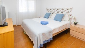 Un dormitorio con cama, escritorio, televisor y ventana con cortinas.