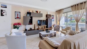 A modern living room with a sofa, armchair, coffee table, TV, and artwork on the walls. - Les Palmiers by Interhome (Le Lavandou)