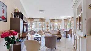 A spacious living area with a sofa, armchairs, a coffee table, and a TV. - Les Palmiers by Interhome (Le Lavandou)