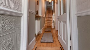 Un couloir avec un escalier en bois, des murs blancs ornés de moulures décoratives et un paillasson à l’entrée.