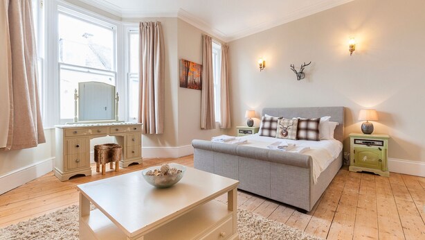Une chambre à coucher avec un lit, des tables de chevet, une commode et une fenêtre avec des rideaux.