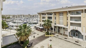 A multi-story hotel with balconies, a marina with boats, and palm trees. - Le Nadir by Interhome (Fréjus)
