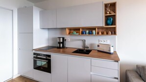 A compact kitchen with white cabinets, a built-in oven, a coffee maker, a toaster, and a shelf with decorative items. - La Spelunca by Interhome (Cargèse)