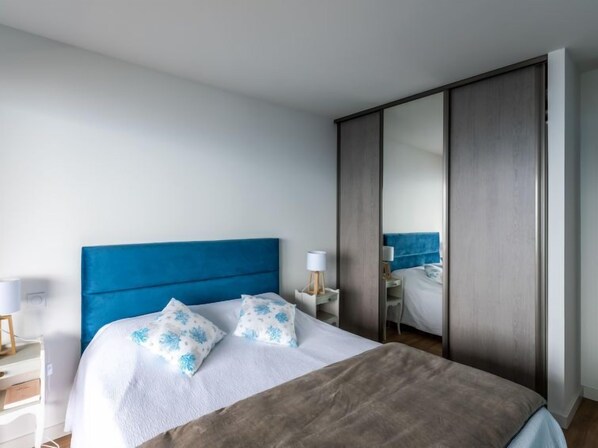 A bedroom with a large bed, a wardrobe, a desk, and a chair.