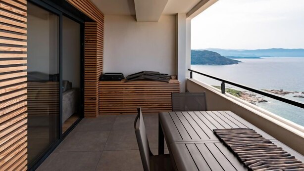 A balcony with a wooden bench, a small table, and a view of the sea. - La Spelunca by Interhome (Cargèse)