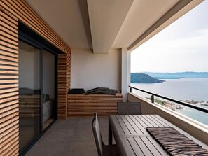 A balcony with a wooden bench, a small table, and a view of the sea.