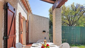 En uteplats med ett bord dukat för middag, omgiven av vita stolar, och en trädörr till vänster.