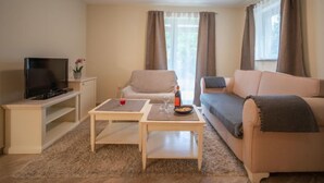Ein Wohnzimmer mit Fernseher, zwei Sofas, einem Couchtisch und einem Fenster mit Vorhängen.