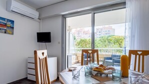 Quarto moderno com uma mesa de jantar, cadeiras, televisão e uma janela grande com vista para edifícios e áreas verdes.