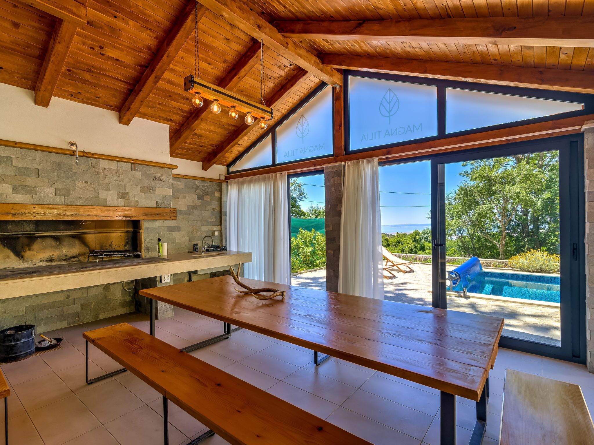 A modern kitchen with a stone backsplash, wooden beams, and a large dining table.