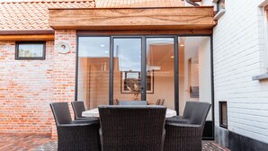 Eine Terrasse im Freien mit Tisch und Stühlen, einer Ziegelwand und einem weißen Gebäude im Hintergrund.