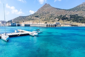 A coastal marina with boats docked, a historic hilltop structure, and buildings with arches. - Holiday Home in Favignana near Cala Rotonda (Favignana)