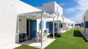 Una hilera de edificios blancos con contraventanas azules, un espacio de estar al aire libre cubierto y un césped bien cuidado.