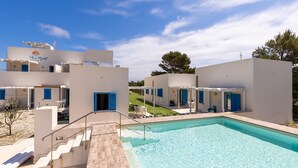 Un resort moderno con piscina, mobiliario exterior y un cielo azul despejado.