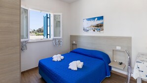 Un dormitorio con una cama grande, una ventana con contraventanas, un cuadro en la pared y una mesita con una silla.