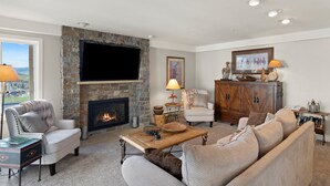 A living room with a stone fireplace, a flat-screen TV, a sofa, a coffee table, and a view of the outdoors. - Ski-in/Out, Walk to Base Area - Torian Plum - Pool& Hot Tubs (Steamboat Springs)