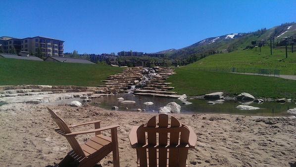 A sandy beach with two wooden chairs facing a river with a stone bridge. - Ski-in/Out, Walk to Base Area - Torian Plum - Pool& Hot Tubs (Steamboat Springs)