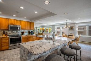 A modern kitchen with wooden cabinets, stainless steel appliances, a marble island, and a dining area with chairs and a table. - Ski-in/Out, Walk to Base Area - Torian Plum - Pool& Hot Tubs (Steamboat Springs)