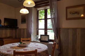 Un comedor con una mesa redonda, sillas, un tazón, un reloj y un televisor sobre una estantería.