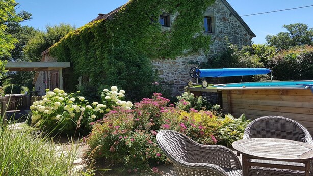 Uma casa de pedra com paredes cobertas de hera, uma piscina e móveis de vime em um jardim.
