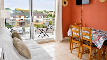 Une chambre avec un lit, un balcon avec une table et des chaises, et un téléviseur fixé au mur.