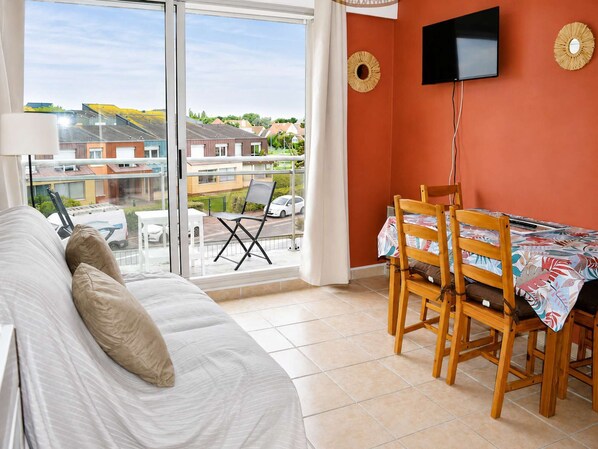 A bedroom with a bed, a balcony with a table and chairs, and a TV mounted on the wall.